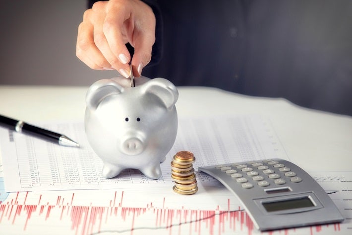 Image of a hand dropping a silver coin into a piggy bank.