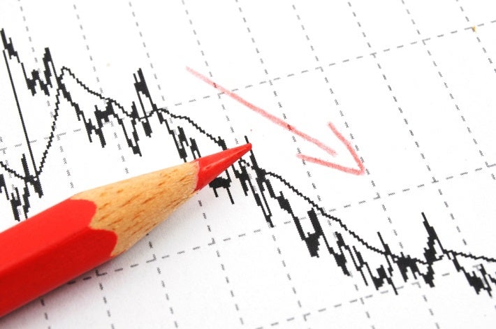 Partial image of a red pencil sitting on a downward trending graph with a red arrow pointing down.