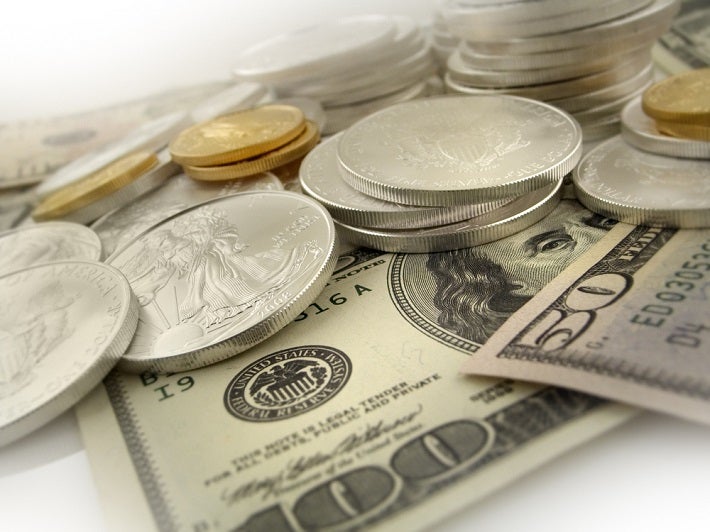 Silver coins loosely stacked on top of US paper money.