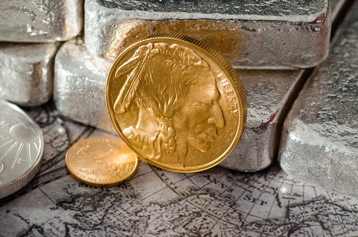 A gold buffalo coin standing against silver bars