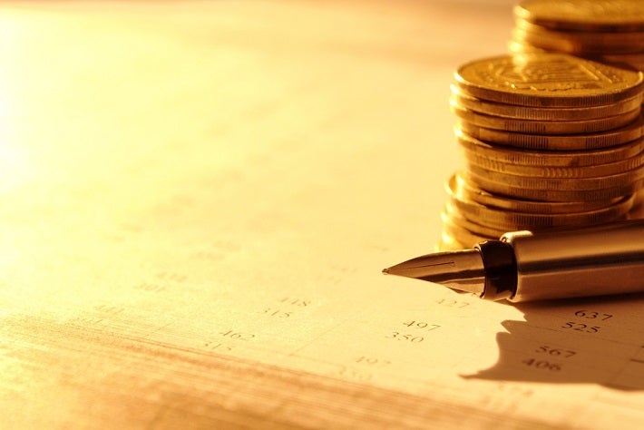 A stack of gold coins behind a gold fine tipped pen